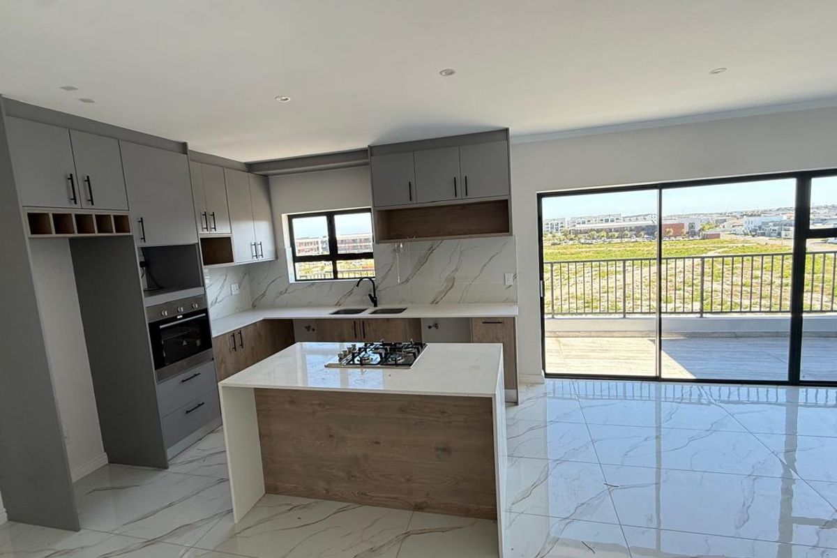 Modern open-plan kitchen featuring a central island with gas hob, sleek cabinetry, marble-look finishes, and direct access to a balcony through sliding glass doors.
