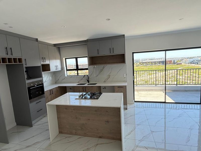 Modern open-plan kitchen featuring a central island with gas hob, sleek cabinetry, marble-look finishes, and direct access to a balcony through sliding glass doors.