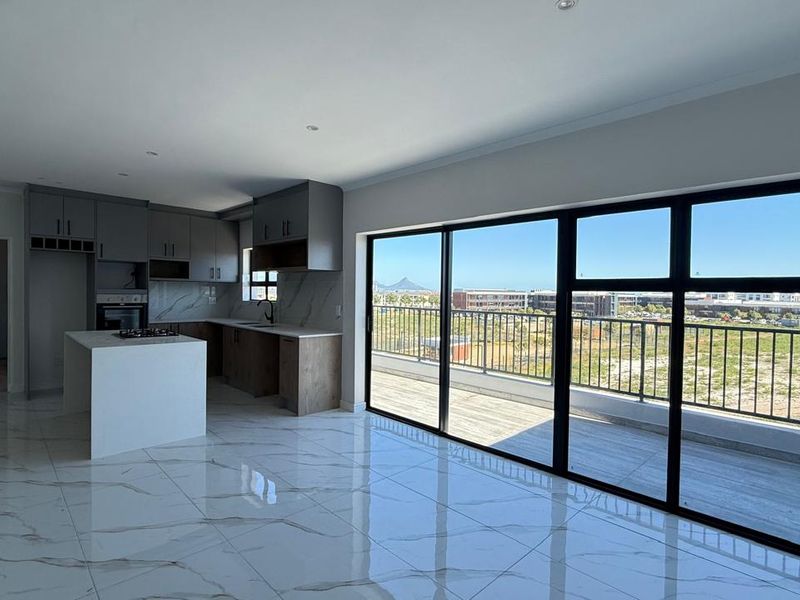 Modern open-plan kitchen and living area featuring marble-look tiled floors, sleek cabinetry, and large sliding doors opening to a balcony with scenic views.
