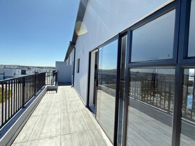 A spacious, modern balcony featuring tiled flooring, a secure metal balustrade, and large sliding glass doors providing seamless indoor-outdoor flow.