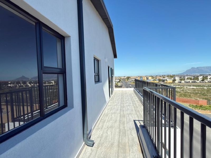 A spacious balcony featuring modern tiled flooring, a secure metal balustrade, and expansive views of the surrounding area and distant mountains.