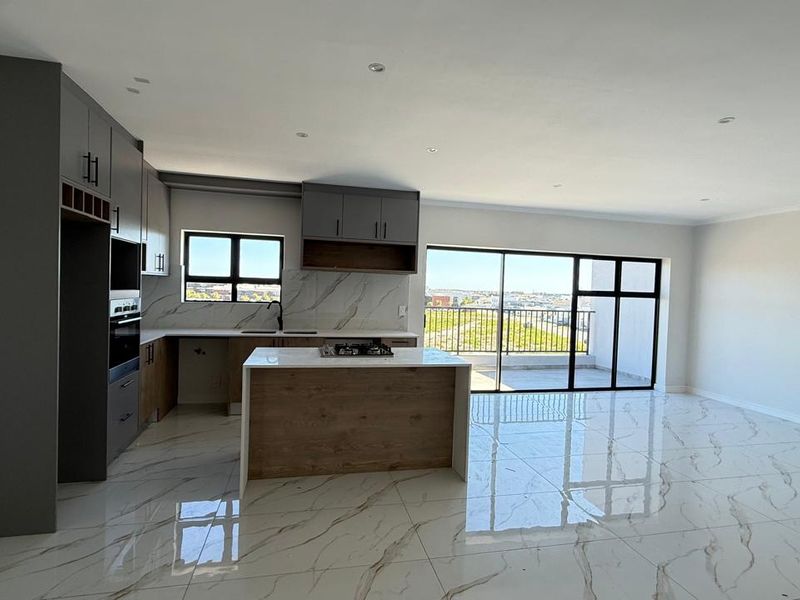 Modern open-plan kitchen and living area featuring marble-look tiled floors, sleek grey cabinetry, a central island with a gas hob, and access to a balcony.