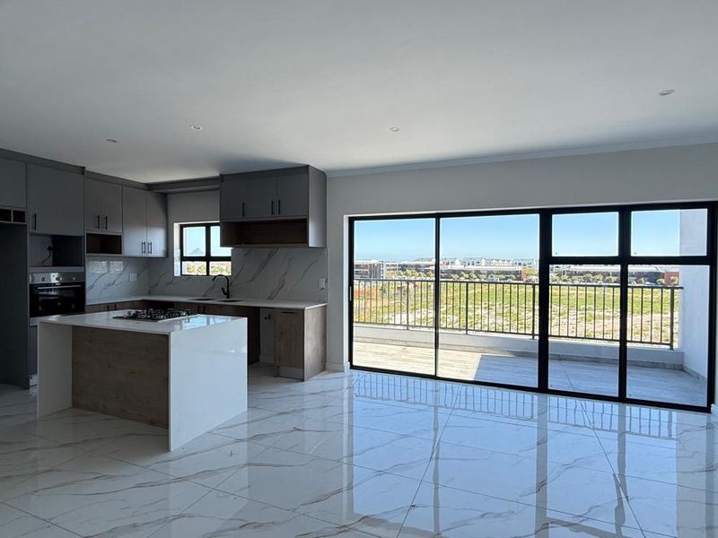 Modern open-plan kitchen and living area featuring sleek cabinetry, stone countertops, marble-look tiled flooring, and large sliding doors leading to a private balcony.