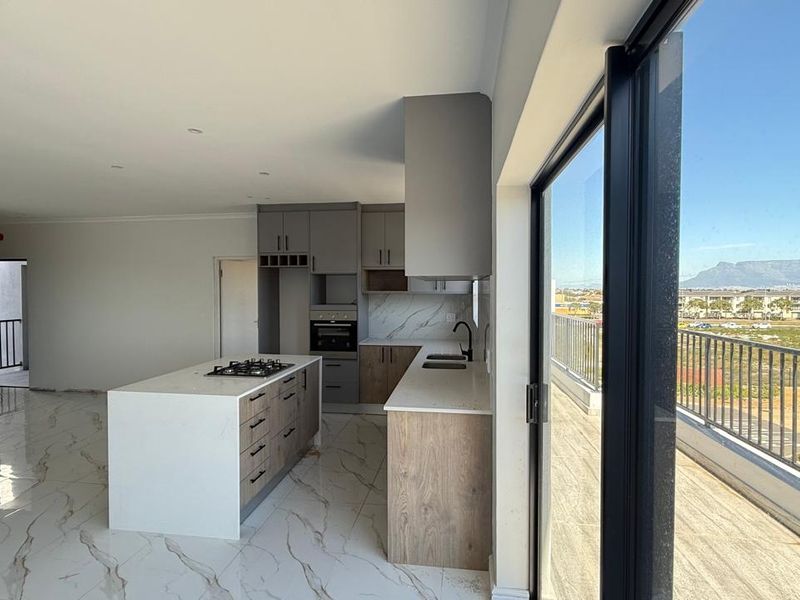 Modern open-plan kitchen featuring a central island, gas hob, and sleek cabinetry, seamlessly flowing onto a balcony with scenic mountain views.