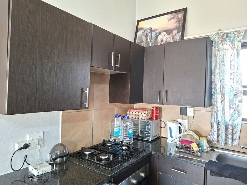 Compact kitchen featuring dark wood cabinetry, granite countertops, a gas hob, built-in oven, and tiled backsplash.