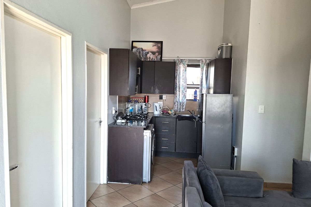 Compact kitchen area featuring dark cabinetry, laminate countertops, and tiled flooring, integrated into an open-plan living space with vaulted ceilings.
