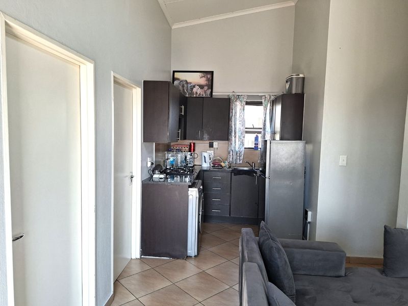 Compact kitchen area featuring dark cabinetry, laminate countertops, and tiled flooring, integrated into an open-plan living space with vaulted ceilings.