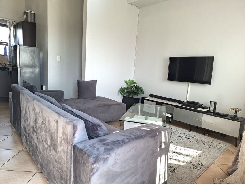 Open plan living area featuring tiled flooring and a wall-mounted television setup, providing a functional space for relaxation and entertainment.
