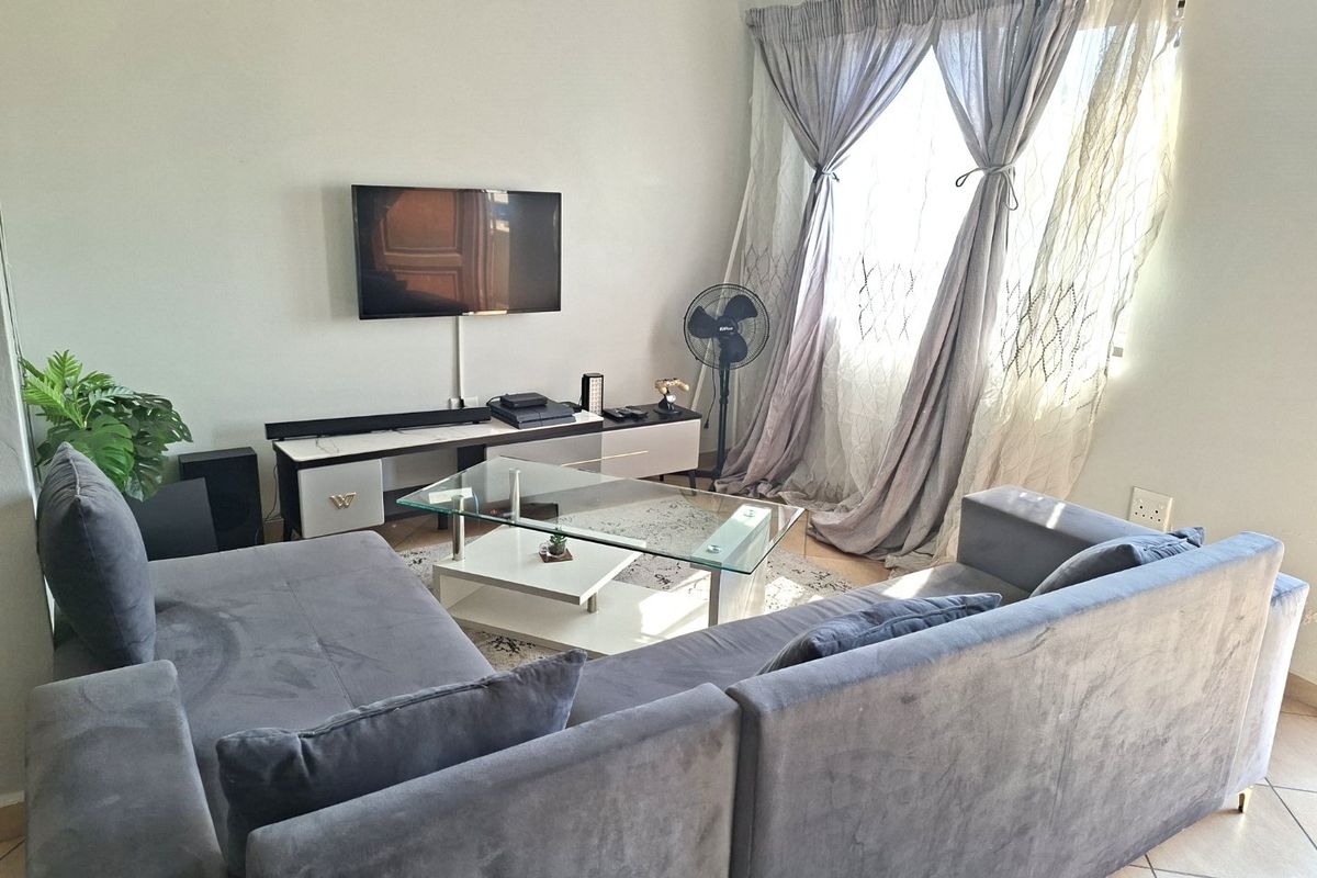 A comfortable living room featuring tiled flooring, large windows with curtains, and wall-mounted television space, offering a functional and well-lit living area.