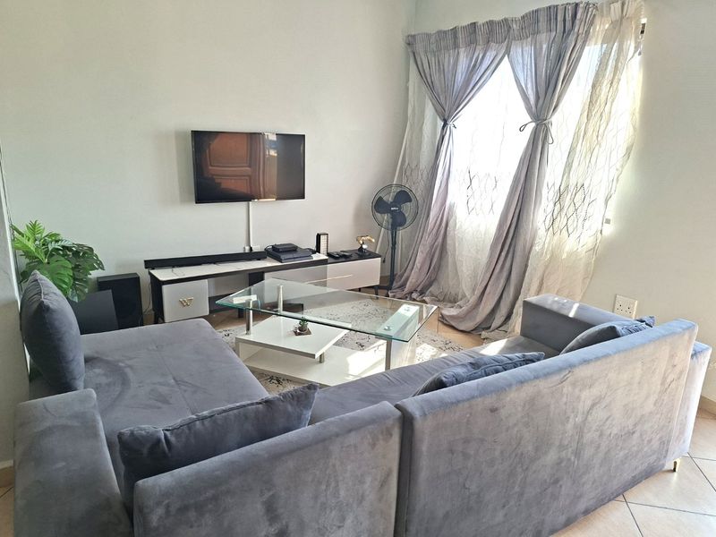 A comfortable living room featuring tiled flooring, large windows with curtains, and wall-mounted television space, offering a functional and well-lit living area.