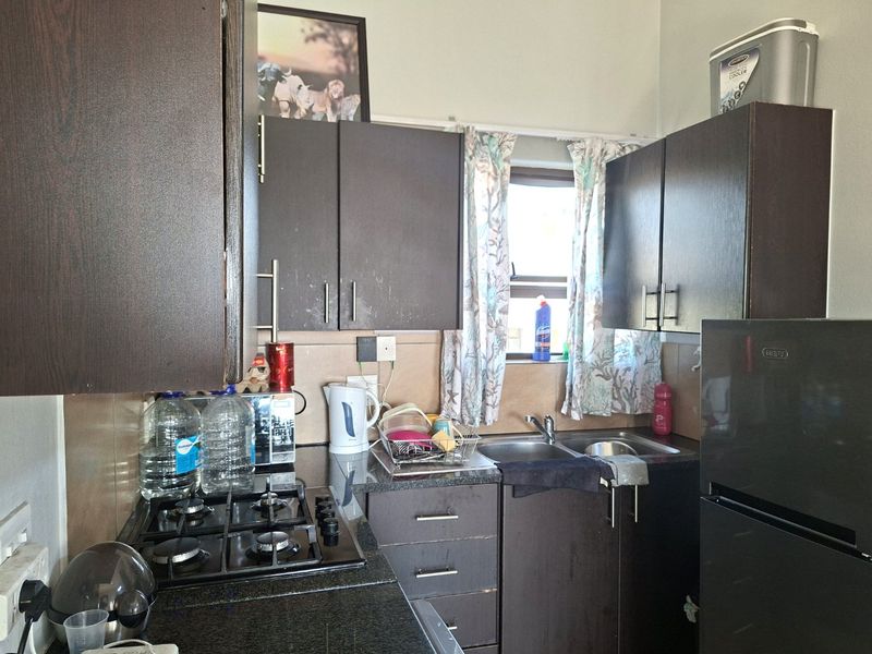Compact kitchen featuring dark wood cabinetry, granite countertops, a gas hob, and a double bowl sink with a tiled splashback.