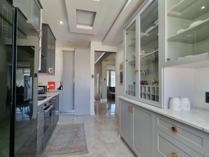 Modern kitchen featuring sleek grey cabinetry, stone countertops, integrated appliances, and elegant glass-fronted display units with recessed ceiling lighting.