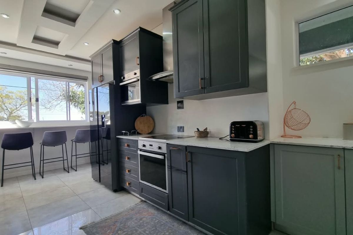 Modern kitchen featuring dark cabinetry, stone countertops, integrated appliances, and a breakfast bar area with natural light.