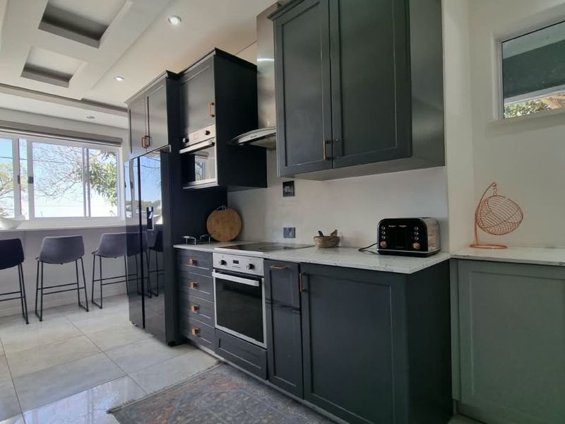 Modern kitchen featuring dark cabinetry, stone countertops, integrated appliances, and a breakfast bar area with natural light.