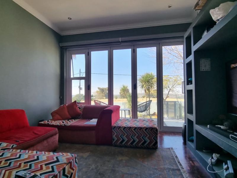 A comfortable living room featuring a large built-in shelving unit and expansive aluminium stacker doors that provide natural light and access to the outdoors.