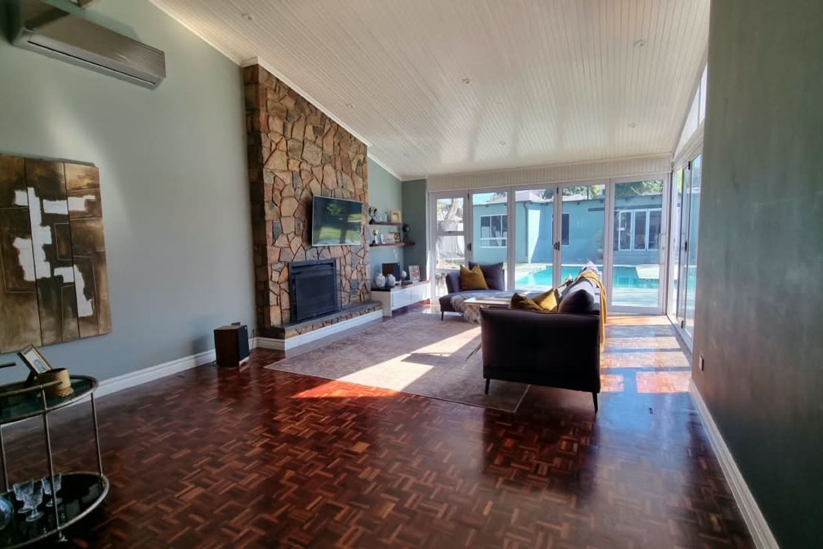 Spacious living room featuring classic parquet flooring, a striking stone fireplace, and large bi-fold doors providing seamless access to the pool area.
