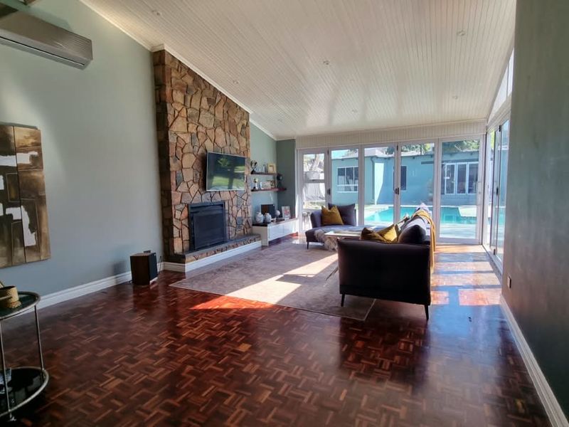 Spacious living room featuring classic parquet flooring, a striking stone fireplace, and large bi-fold doors providing seamless access to the pool area.