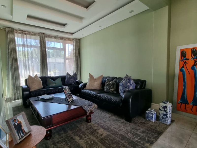 A comfortable living room featuring a recessed ceiling with downlights, large windows allowing natural light, and neutral tiled flooring.