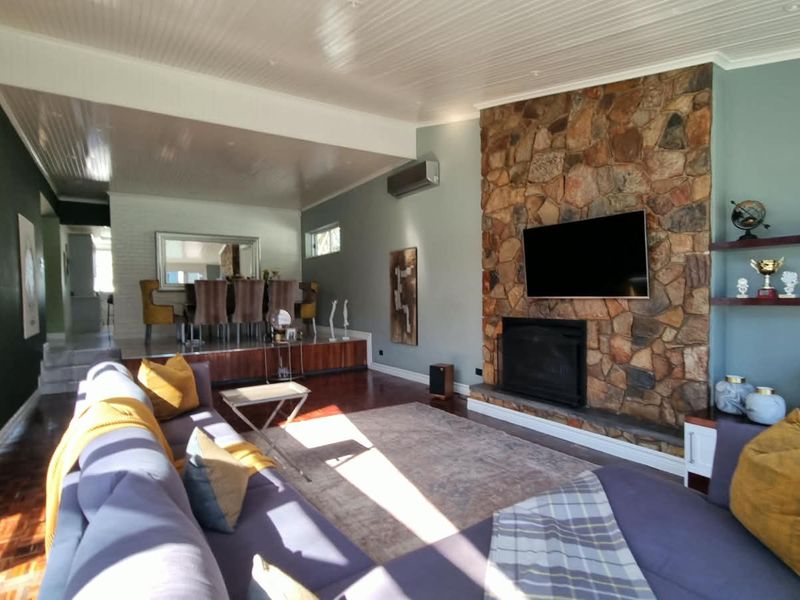 Spacious open-plan living and dining area featuring a prominent stone fireplace, parquet flooring, and a raised dining platform with modern finishes.