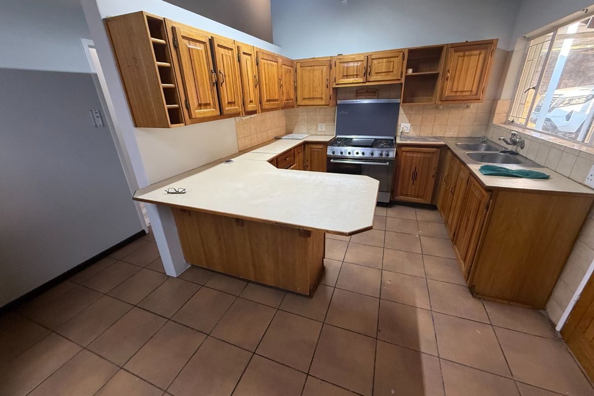 A functional kitchen featuring wooden cabinetry, laminate countertops, a freestanding gas stove, and a double basin sink with tiled flooring and backsplash.