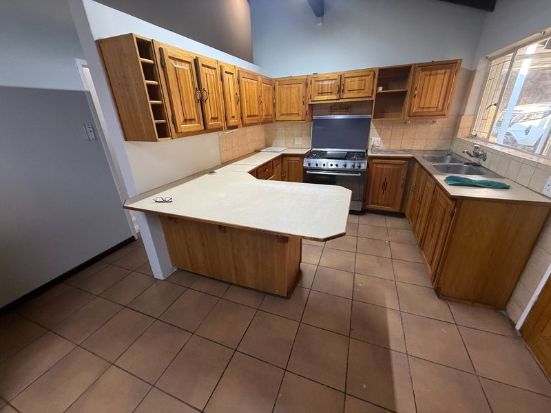 A functional kitchen featuring wooden cabinetry, laminate countertops, a freestanding gas stove, and a double basin sink with tiled flooring and backsplash.