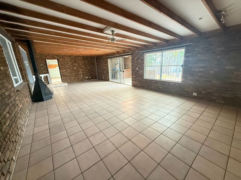 Spacious living area featuring exposed timber ceiling beams, rustic brick walls, ceramic tiled flooring, and a freestanding fireplace with direct access to the patio.