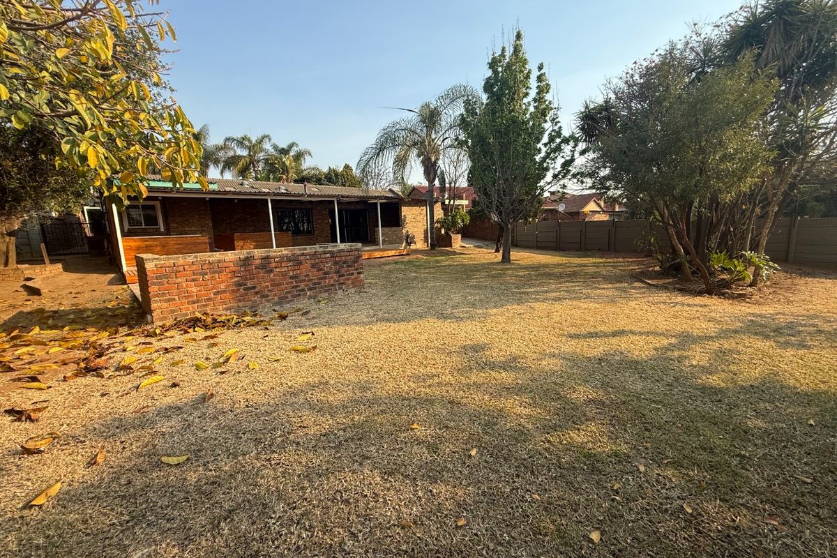 Spacious rear garden featuring a covered patio with wooden decking, a low brick wall, and established trees within a fenced yard.