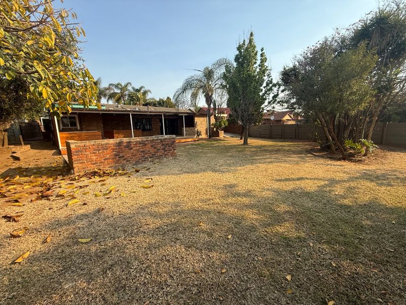 Spacious rear garden featuring a covered patio with wooden decking, a low brick wall, and established trees within a fenced yard.