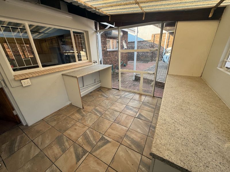 A functional scullery or utility area featuring tiled flooring, laminate countertops, and direct access to the rear paved courtyard.