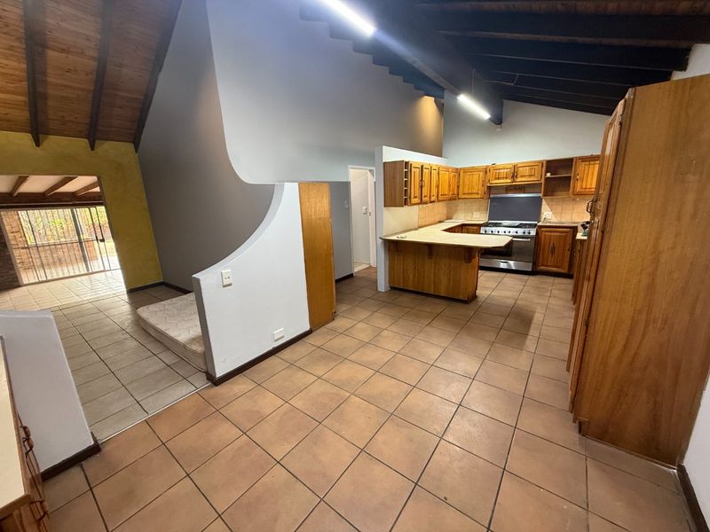 Open plan kitchen area featuring exposed timber beams, wooden cabinetry, and a gas stove, leading to an adjacent living space with tiled flooring.