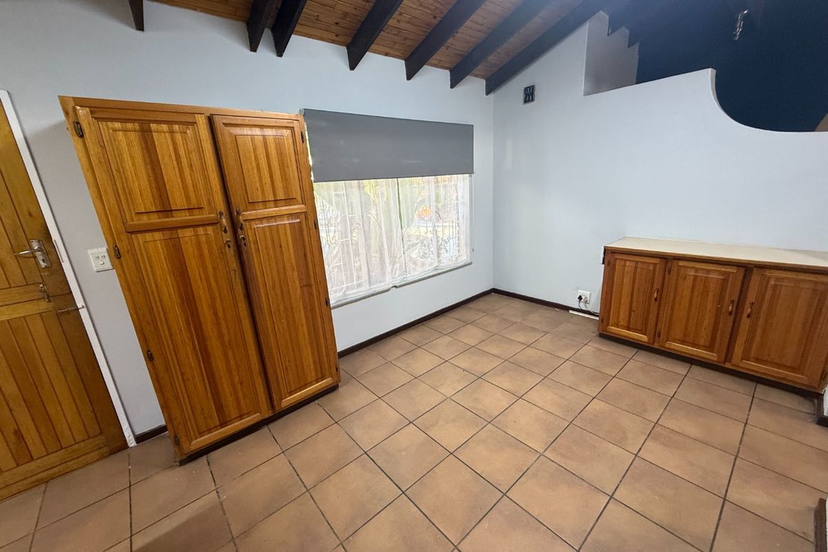 A bedroom featuring exposed timber ceiling beams, tiled flooring, and built-in wooden cabinetry, offering a functional space with potential for modern updates.