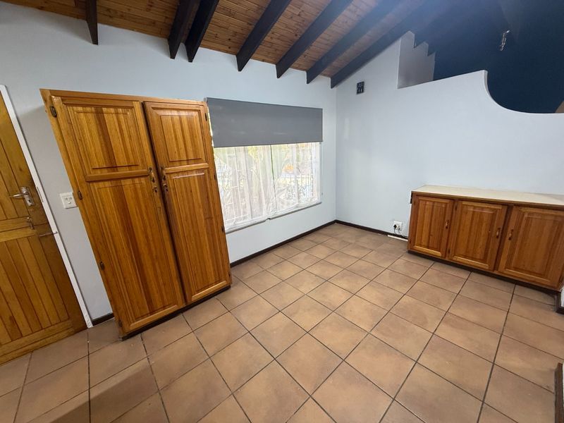 A bedroom featuring exposed timber ceiling beams, tiled flooring, and built-in wooden cabinetry, offering a functional space with potential for modern updates.