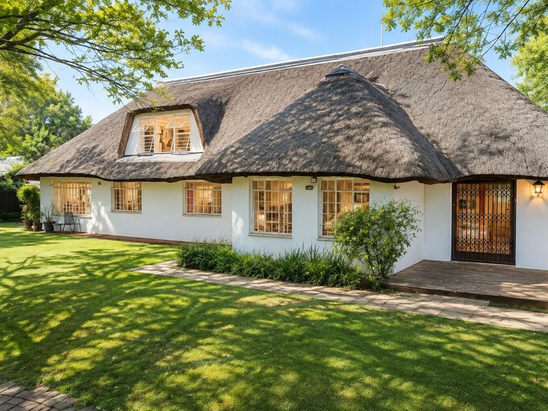 A charming cottage-style home featuring a traditional thatched roof, timber decking, and a well-maintained garden with a paved walkway.