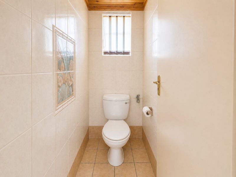 A compact, tiled guest toilet featuring a white ceramic toilet suite, decorative wall accents, and a small window with security bars.