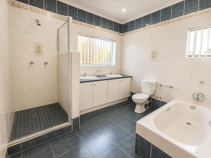 A spacious bathroom featuring a walk-in shower, dual vanity with storage, a built-in bathtub, and tiled finishes throughout.