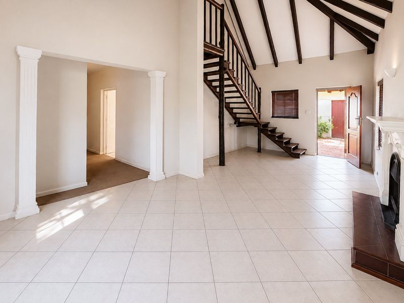 Spacious living area featuring high vaulted ceilings with exposed timber beams, tiled flooring, a built-in fireplace, and a feature timber staircase.