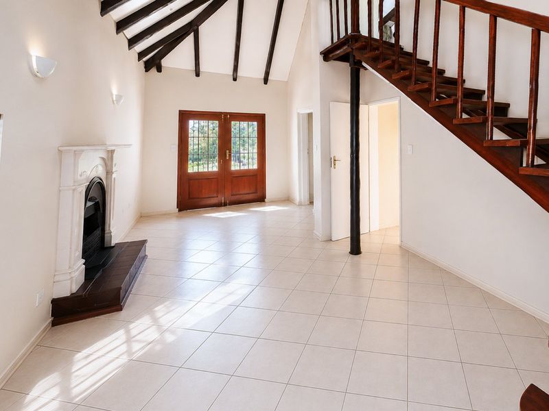 Spacious living area featuring high vaulted ceilings with exposed timber beams, a classic fireplace, tiled flooring, and a wooden staircase leading to the upper level.