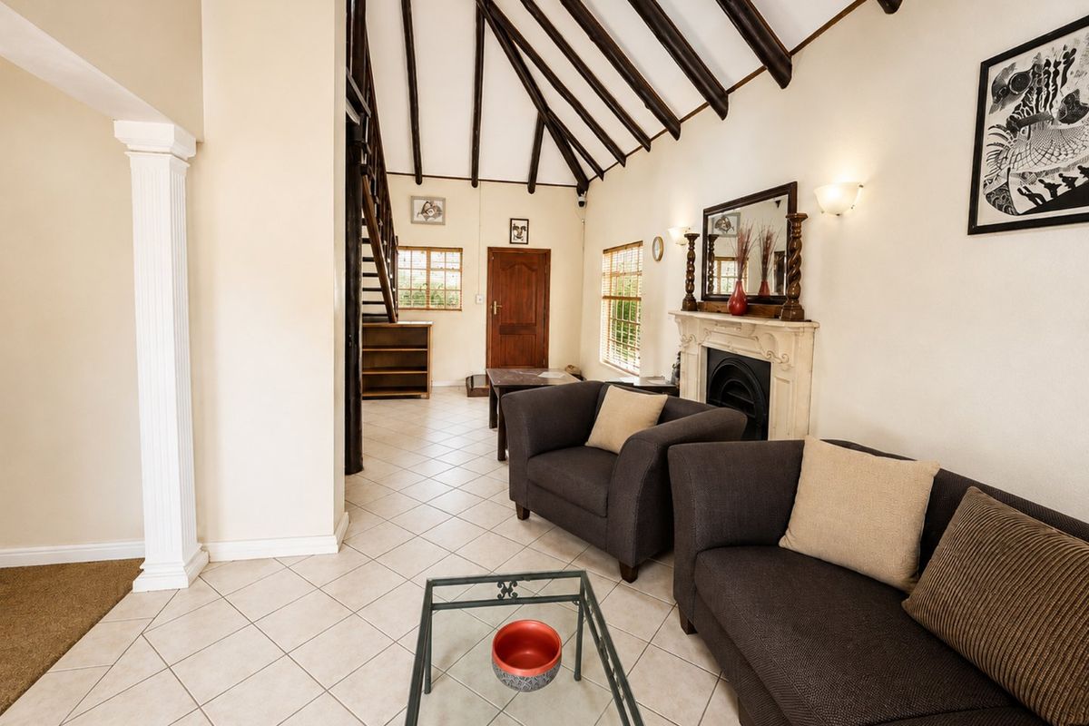 Spacious living room featuring a vaulted ceiling with exposed timber beams, tiled flooring, and a classic fireplace with a mantelpiece.