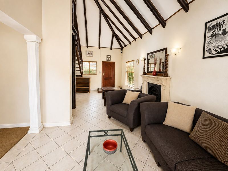 Spacious living room featuring a vaulted ceiling with exposed timber beams, tiled flooring, and a classic fireplace with a mantelpiece.
