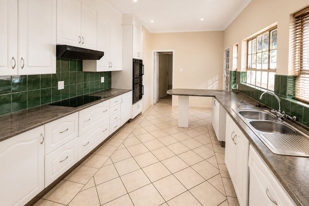 Spacious kitchen featuring white cabinetry, dark laminate countertops, green tiled splashbacks, built-in double oven, electric hob, and tiled flooring.