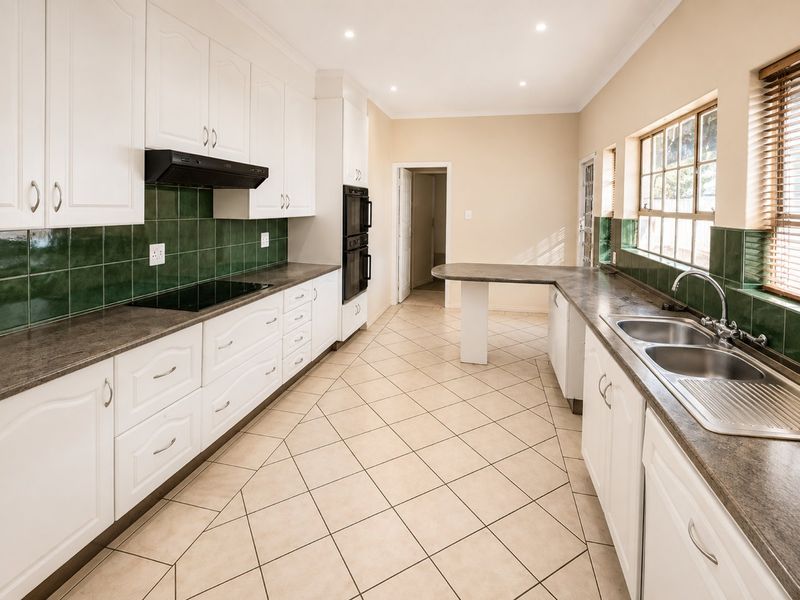 Spacious kitchen featuring white cabinetry, dark laminate countertops, green tiled splashbacks, built-in double oven, electric hob, and tiled flooring.