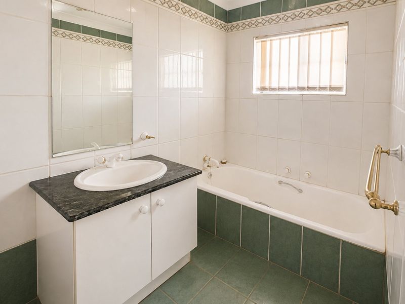 A clean, functional bathroom featuring a vanity with a granite countertop, a built-in bathtub, and classic green and white wall and floor tiling.