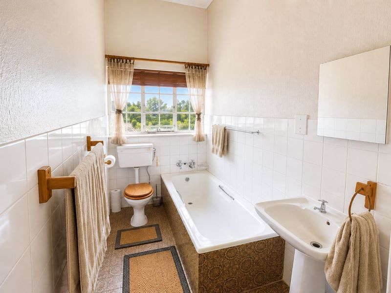 A functional bathroom featuring a pedestal basin, built-in bathtub, and classic white wall tiling with a window providing natural light.