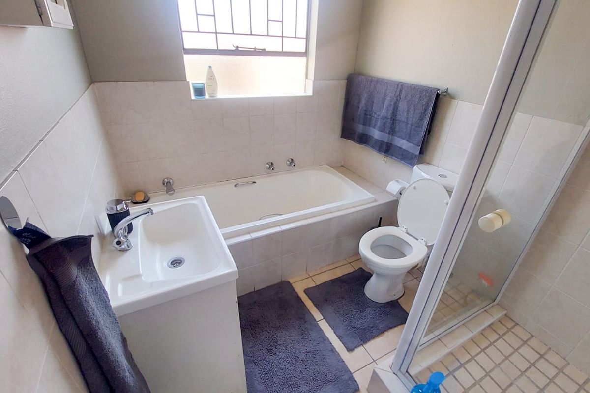 A functional bathroom featuring a built-in bathtub, separate shower enclosure, pedestal sink, and toilet with tiled finishes throughout.