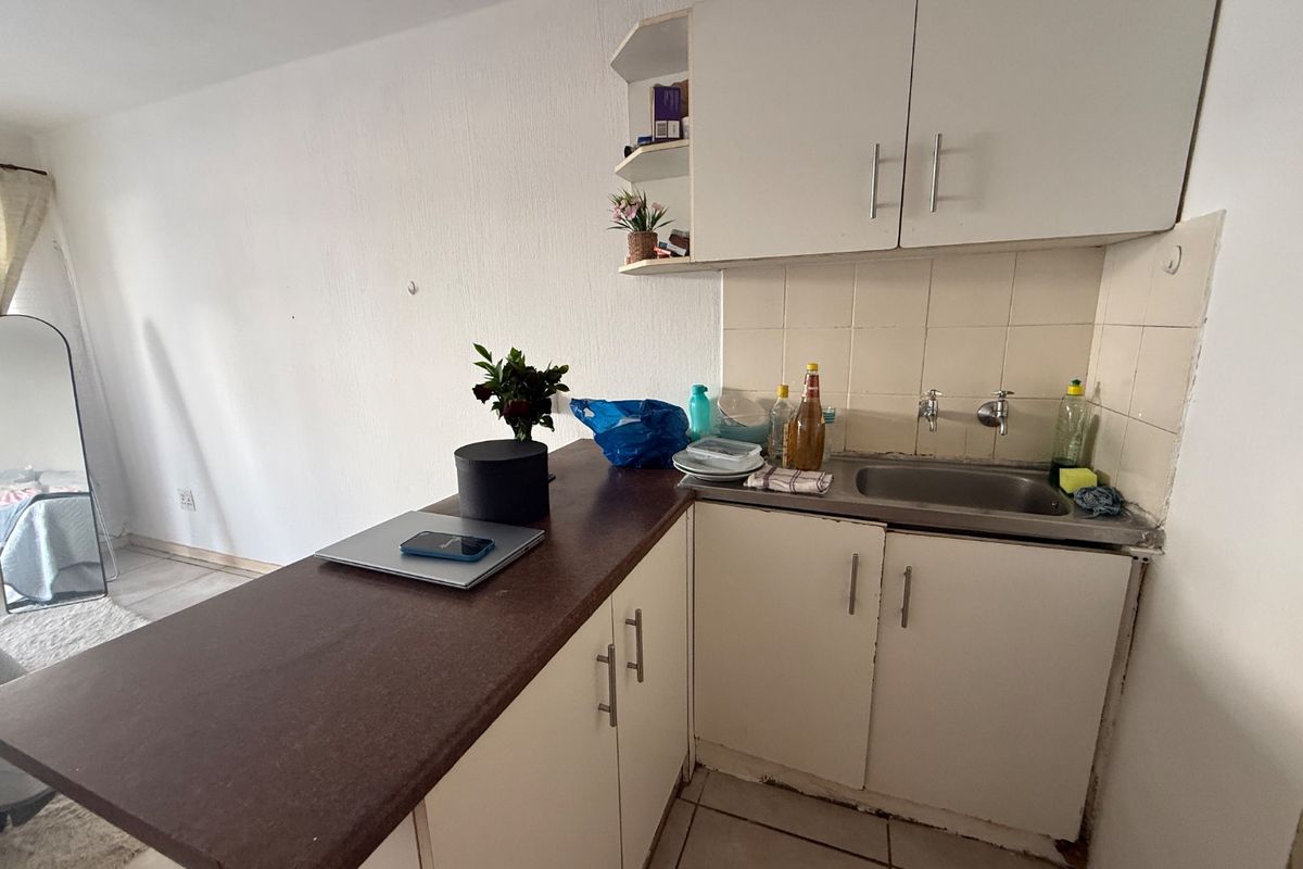 Compact kitchen area featuring laminate countertops, built-in cabinetry, and a stainless steel sink, requiring some cosmetic updates to improve its overall condition.