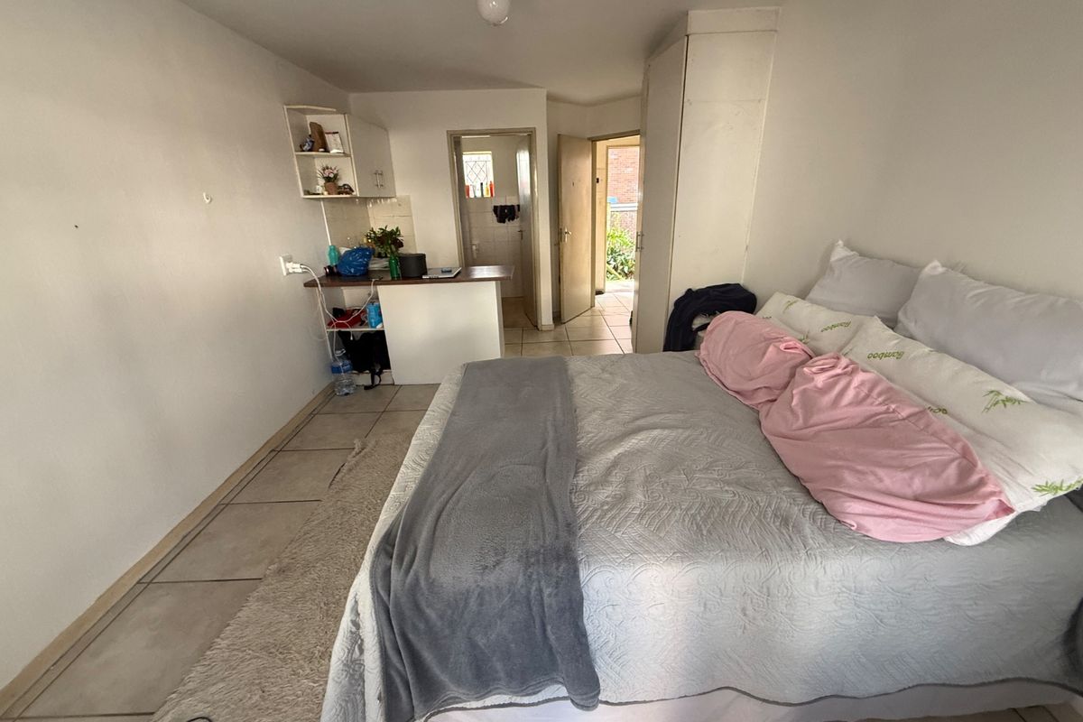 A compact bedroom featuring tiled flooring, a built-in cupboard, and an integrated kitchenette area with direct access to an adjacent room.