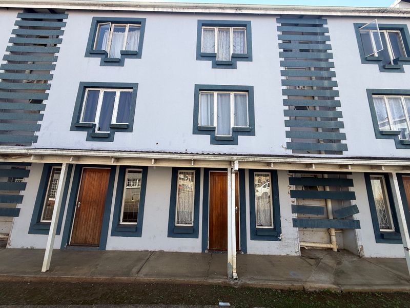 Front elevation of a multi-story apartment building featuring timber entrance doors, aluminium windows, and a covered ground-level walkway.