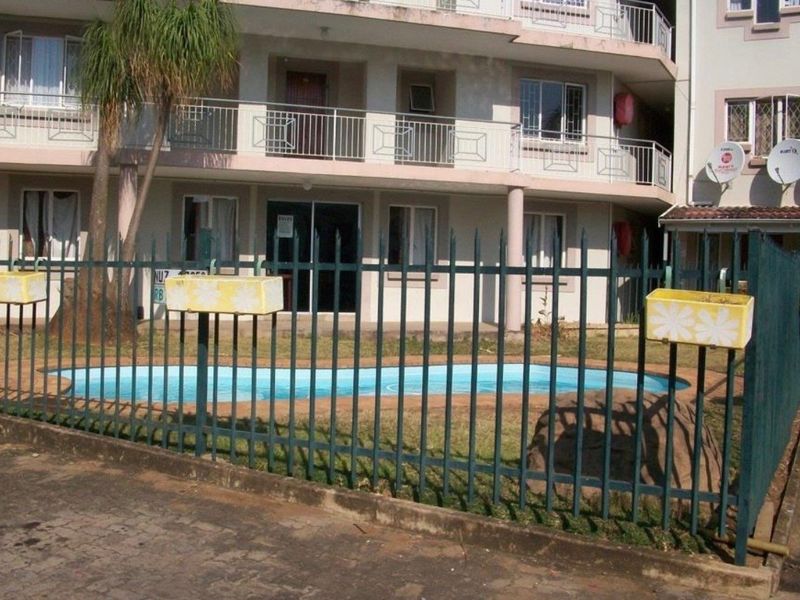 Exterior view of an apartment building featuring a swimming pool, security fencing, and balcony access.