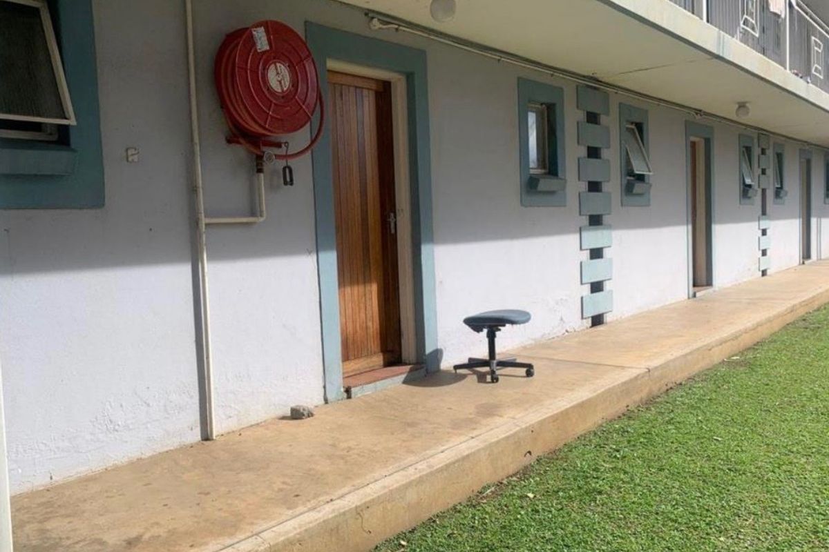 Exterior view of an apartment building walkway featuring a fire hose reel, timber entrance door, and concrete pathway adjacent to a lawn area.