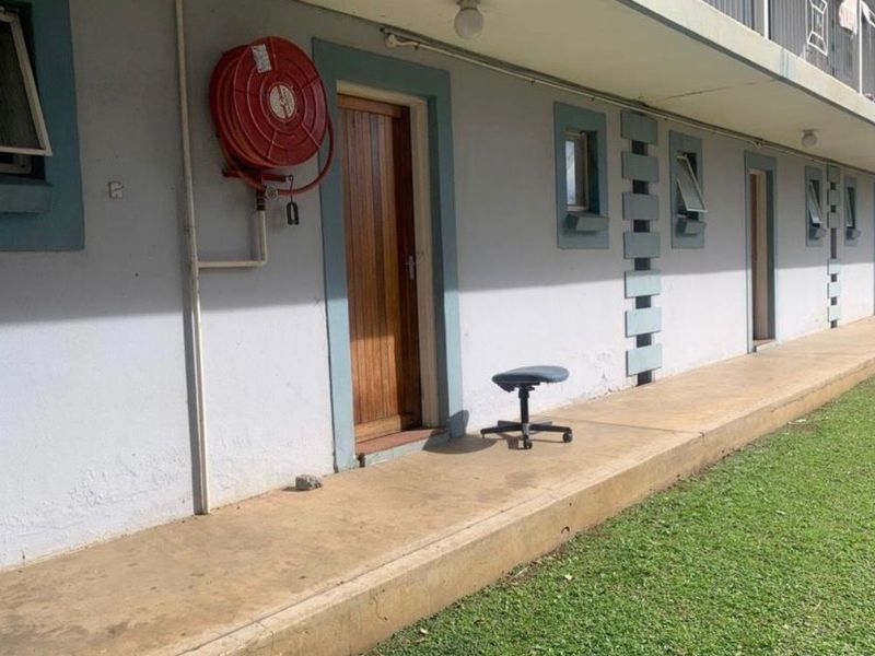Exterior view of an apartment building walkway featuring a fire hose reel, timber entrance door, and concrete pathway adjacent to a lawn area.